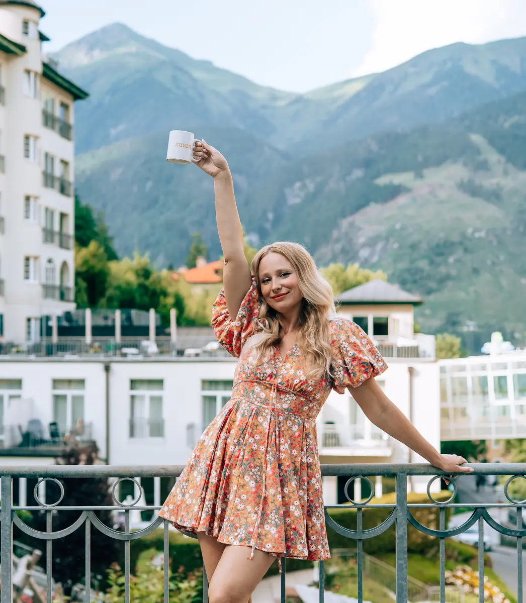 Elena raising a mug on a balcony overlooking the Austrian mountains