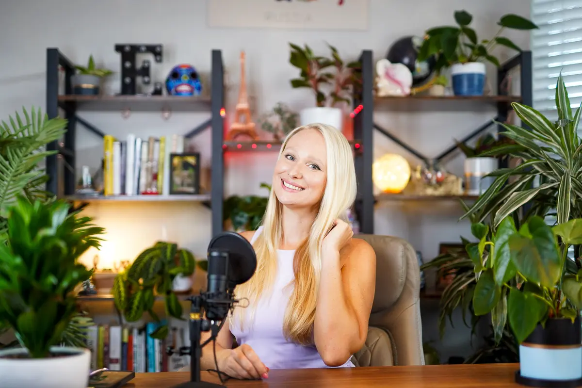 Elena seated at her desk with a microphone, surrounded by plants and books