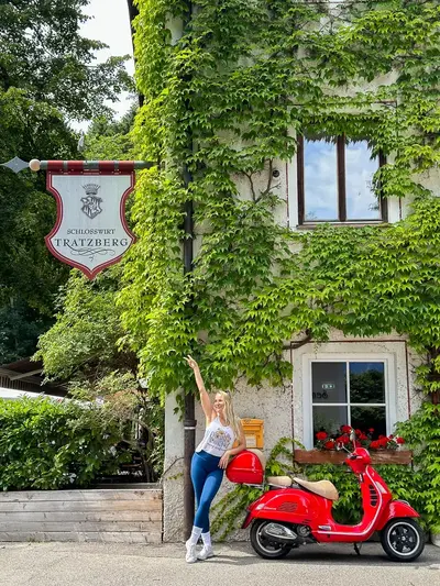 Elena beside a red scooter and ivy-covered building