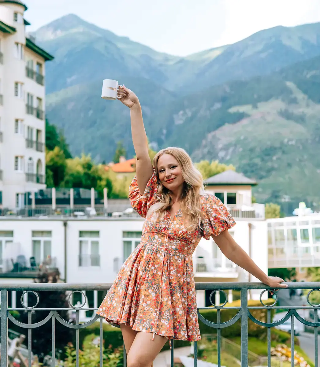 Elena holding a coffee cup high in front of the mountains
